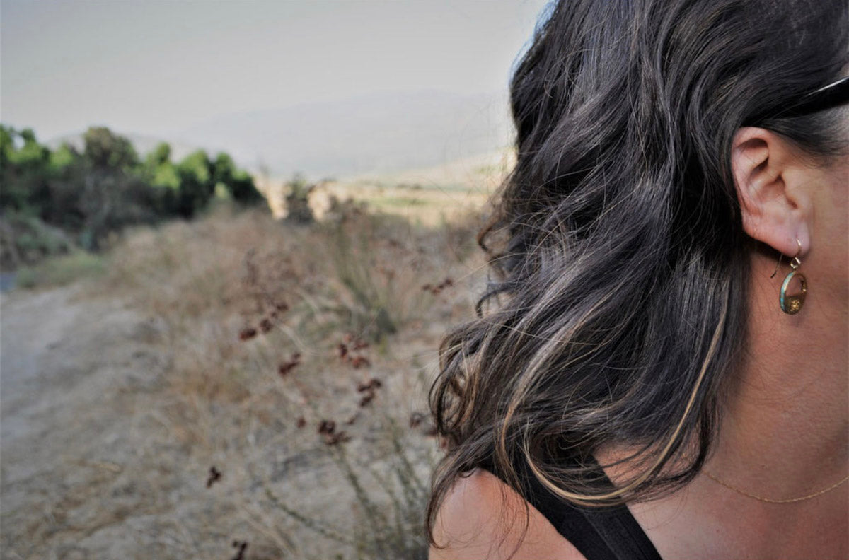 Belle Starr rustic patina earrings with turquoise inlay worn by model in profile, with natural greenery in the background