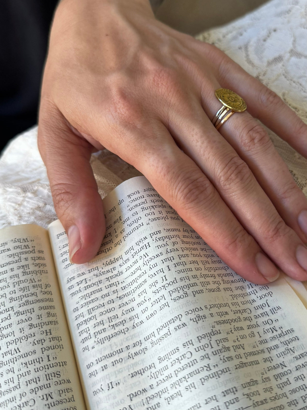 Woman's hand wearing mixed metal rings on book and lace background