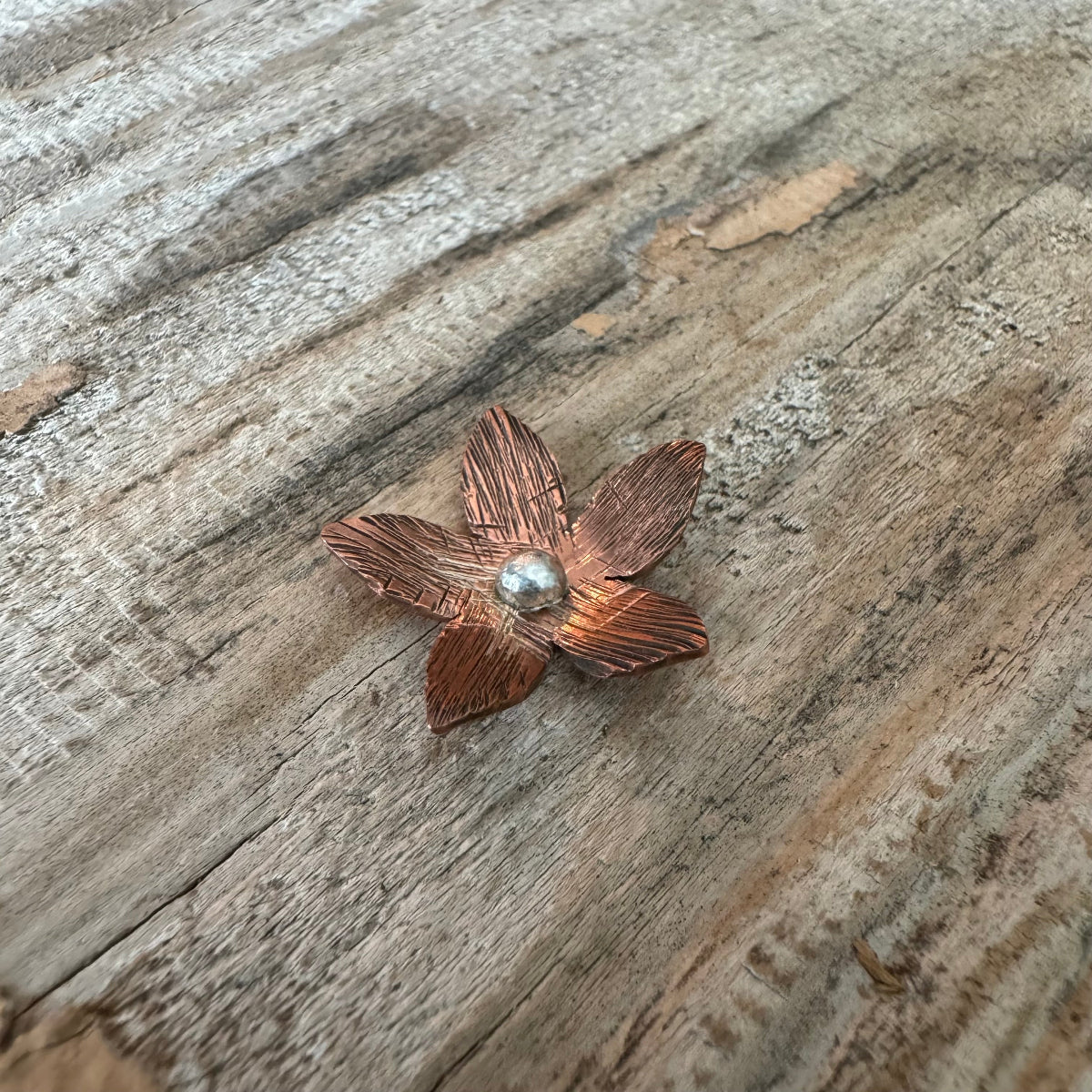 Handforged copper and sterling silver Luella floret centerpiece displayed on rustic wood, awaiting custom ring band design