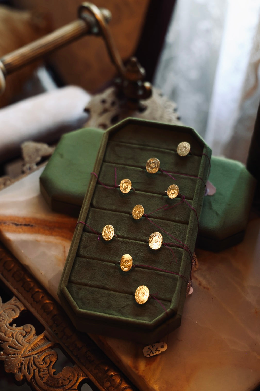 Green velvet ewelry box with brass and sterling silver rings on a decorative surface