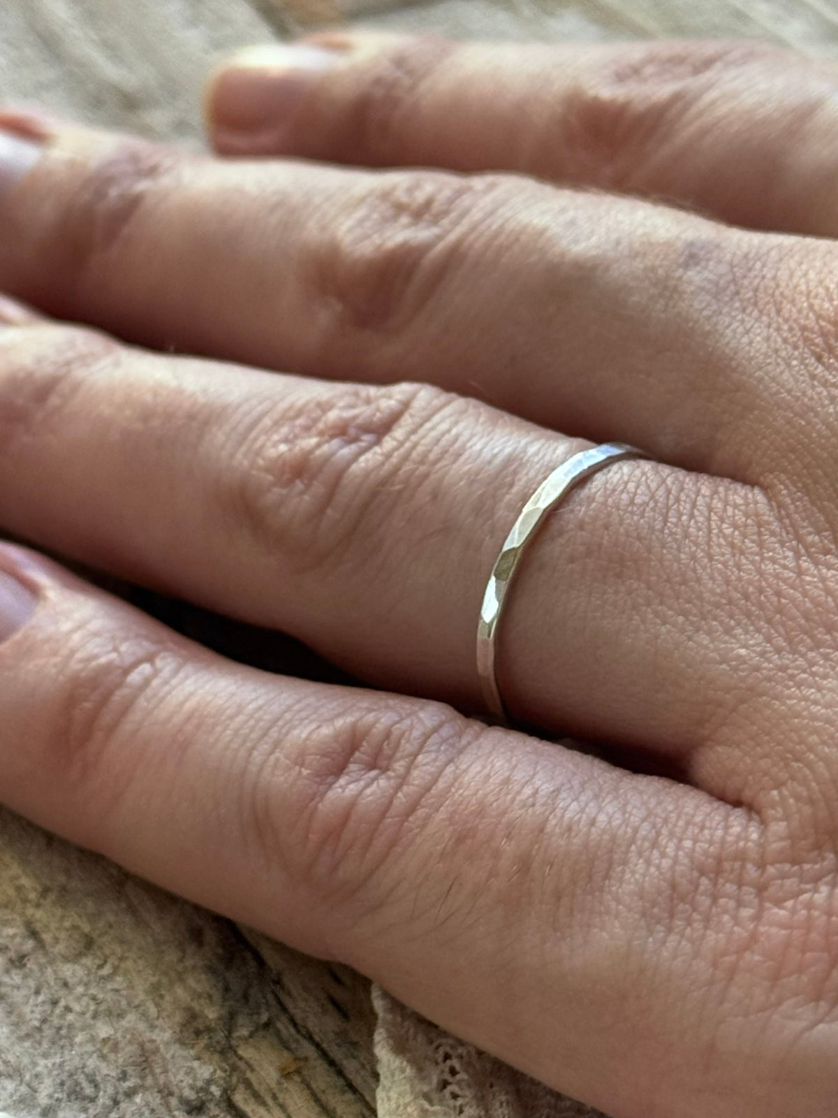 Woman's hand wearing single hammered sterling silver stacking ring on lace and wood background