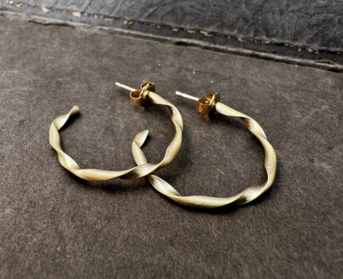 Pair of twisted brass hoop earrings on a textured gray surface