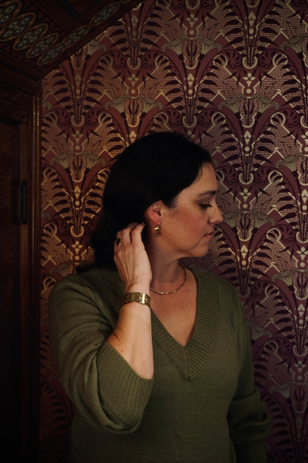 Woman adjusting an earring against a patterned wall.