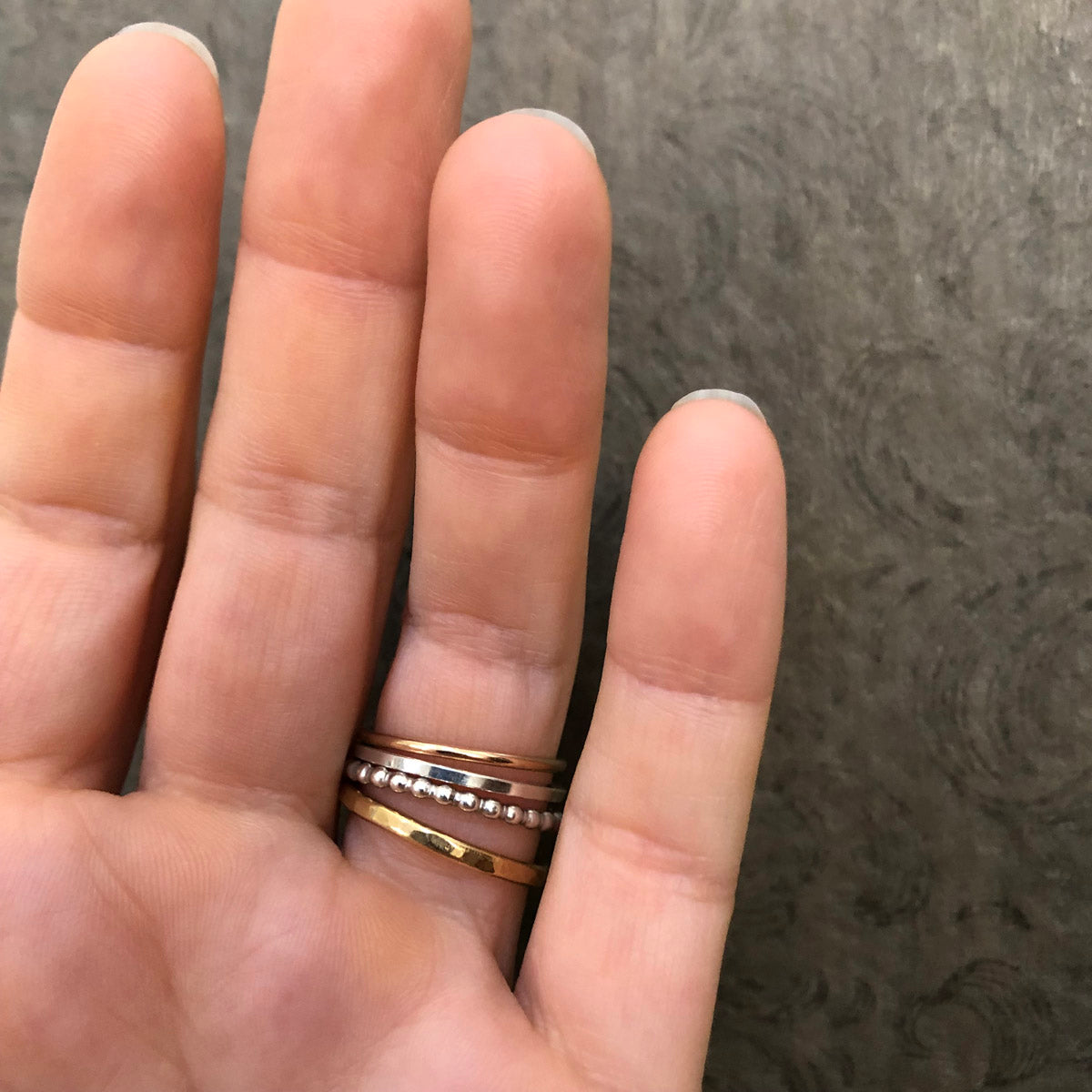 Alpine Loop stacking ring set worn on a hand—four mixed metal rings including hammered brass, gold-filled, and sterling silver bands styled together, handcrafted by Narrow-Gauge Designs