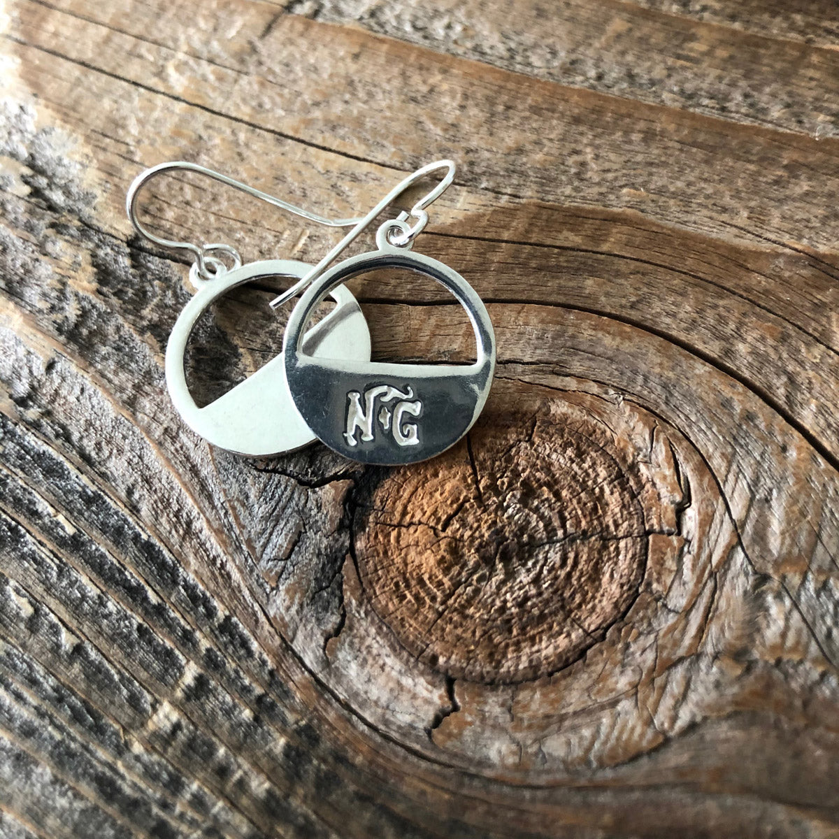 Billy the Kid sterling silver minimalist earrings resting on weathered wooden surface, showcasing smooth silver discs and handcrafted details.