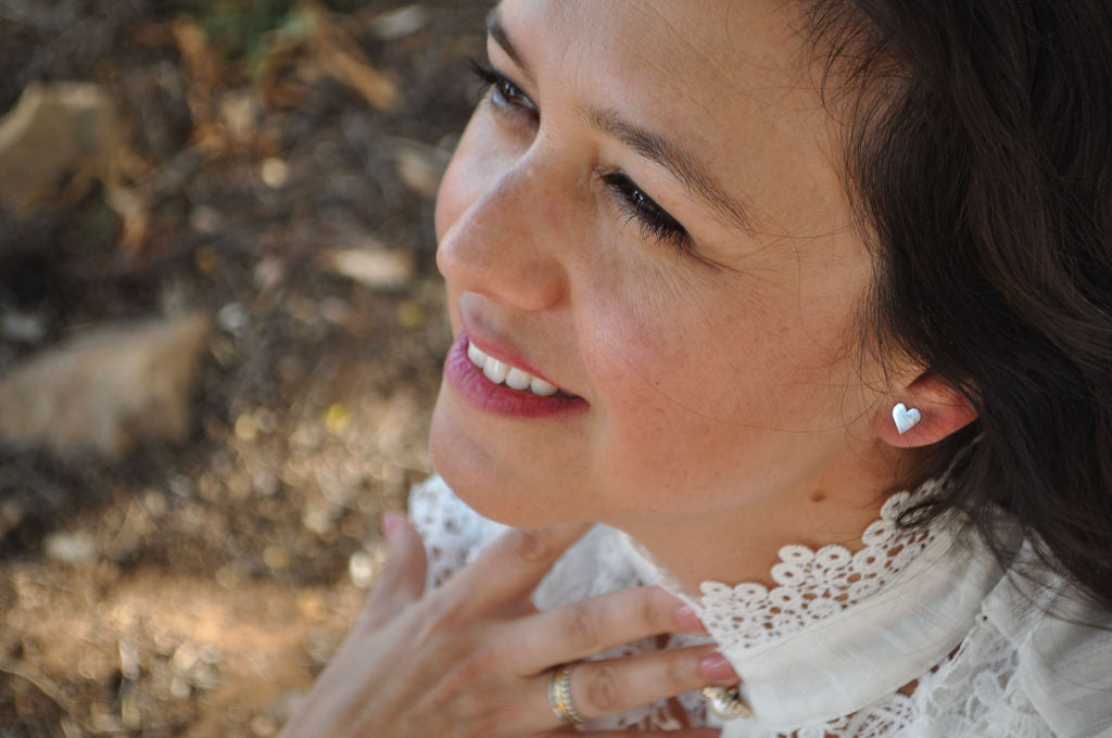 Close-up of model wearing a Heart Pharo sterling silver earring with a white crocheted top, standing in front of a whitewashed building