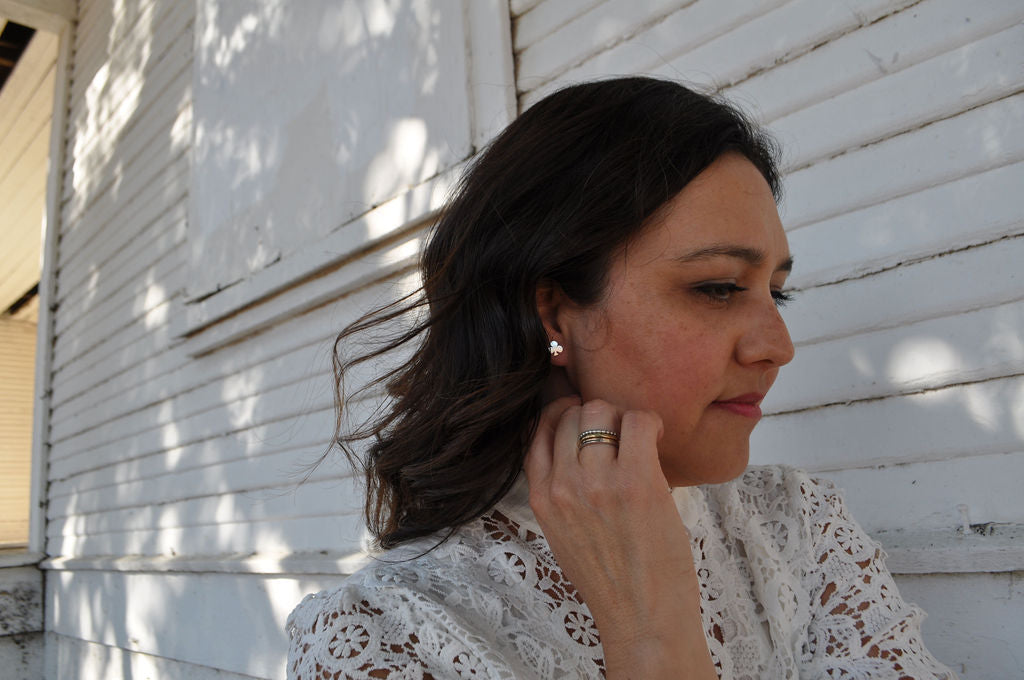 Model wearing Pharo club sterling silver earring and Alpine Loop ring set, dressed in a white crocheted top, standing in front of an old whitewashed building.