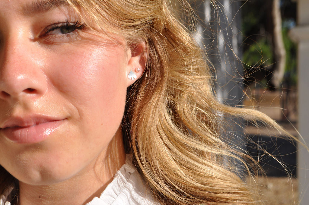Model wearing a spade-shaped Pharo sterling silver earring, looking thoughtfully to the side with hair tucked behind the ear.
